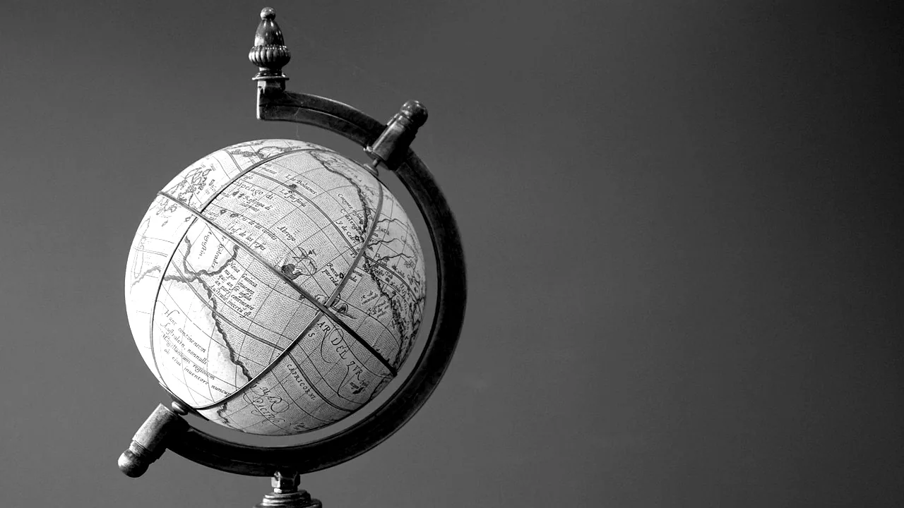 Globe terrestre ancien sur son support, devant un mur uni